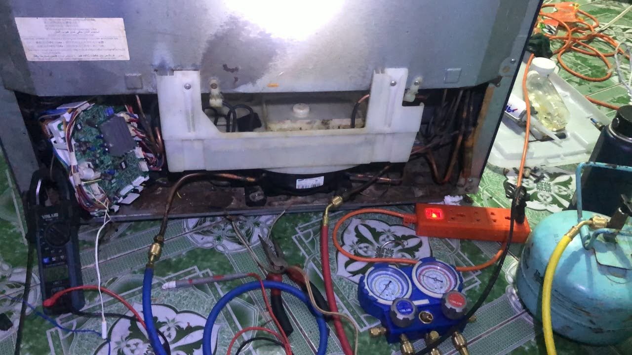 Quá trình kết nối đồng hồ đo áp suất và bình chứa để thực hiện nạp gas, kiểm tra hệ thống làm lạnh phía sau tủ.